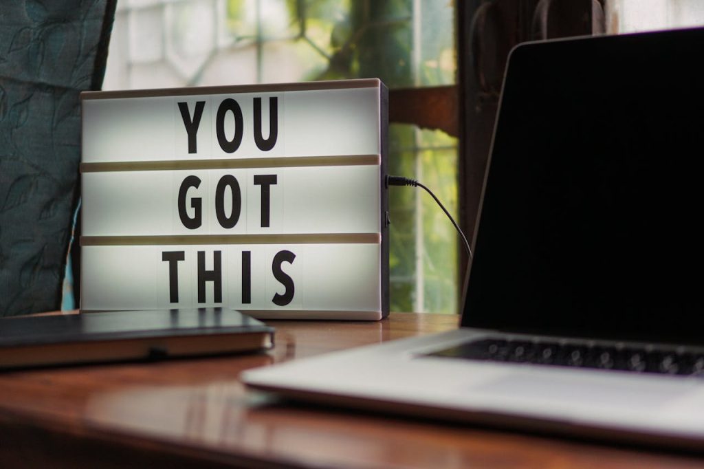 black-and-white-laptop-2740956 Lit sign with You Got This alongside laptop on office desk.